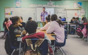 A teacher, standing at the front of the classroom, teaches students 